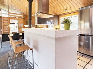 A modern kitchen with a central island, stainless steel appliances, and a wooden ceiling.