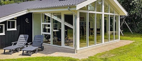 A modern house with a glass-enclosed porch, a chimney, and a lawn with two lounge chairs.