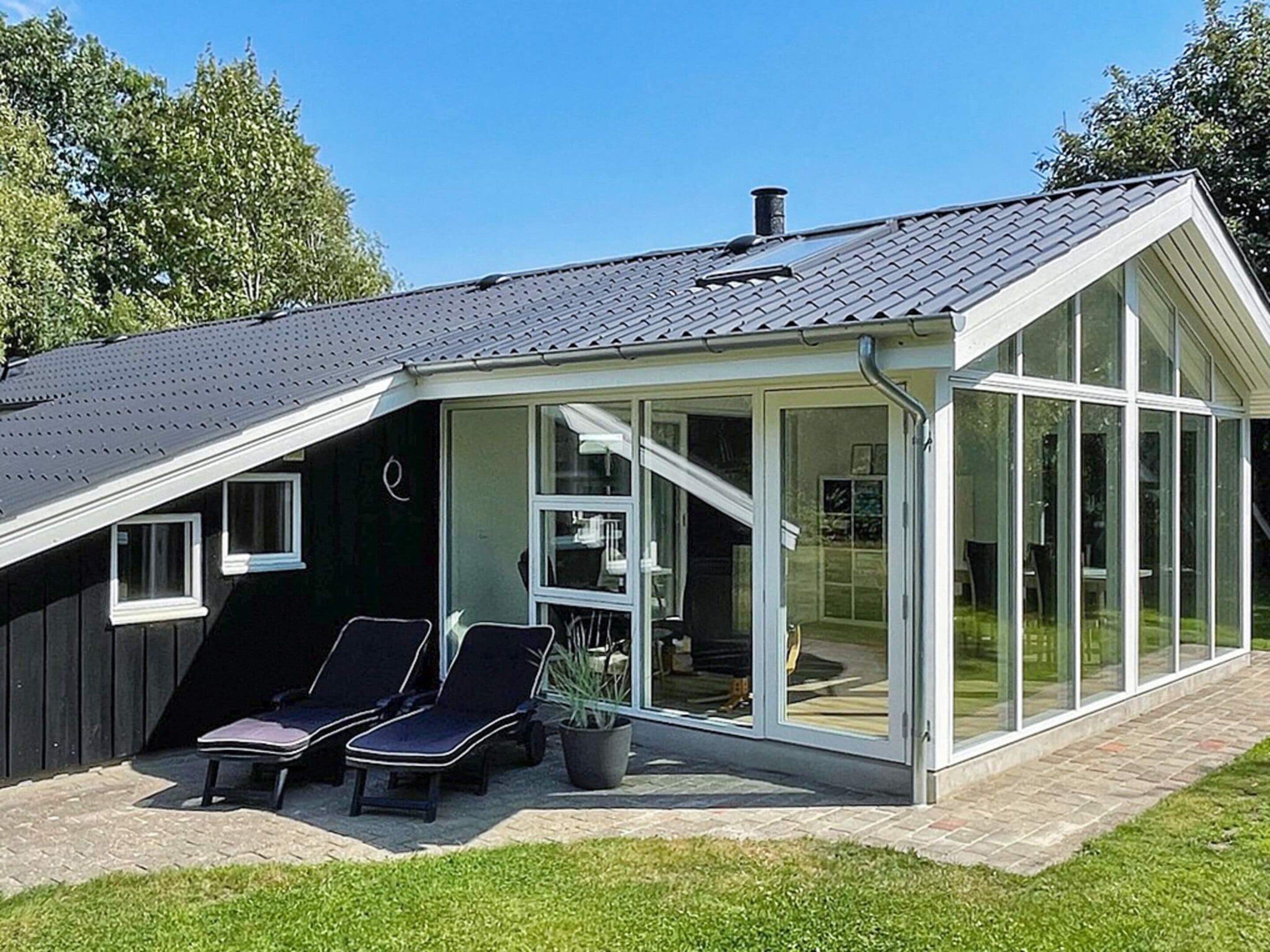A modern house with a sloped roof, a glass conservatory, and two lounge chairs outside.