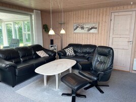 Una habitación con un sofá de cuero negro, una mesa de centro blanca y una silla de escritorio negra. Hay dos lámparas colgantes del techo.