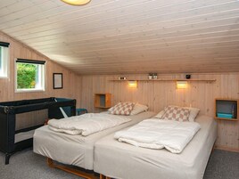 Una habitación con dos camas, una cuna, paredes de madera y una ventana.