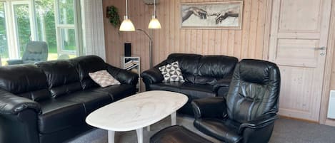 A modern living room with a black leather sofa, a white coffee table, and a black leather armchair. There are two pendant lights hanging from the ceiling.