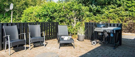 An outdoor patio with a barbecue grill, two wicker chairs, a small table, and a potted plant.