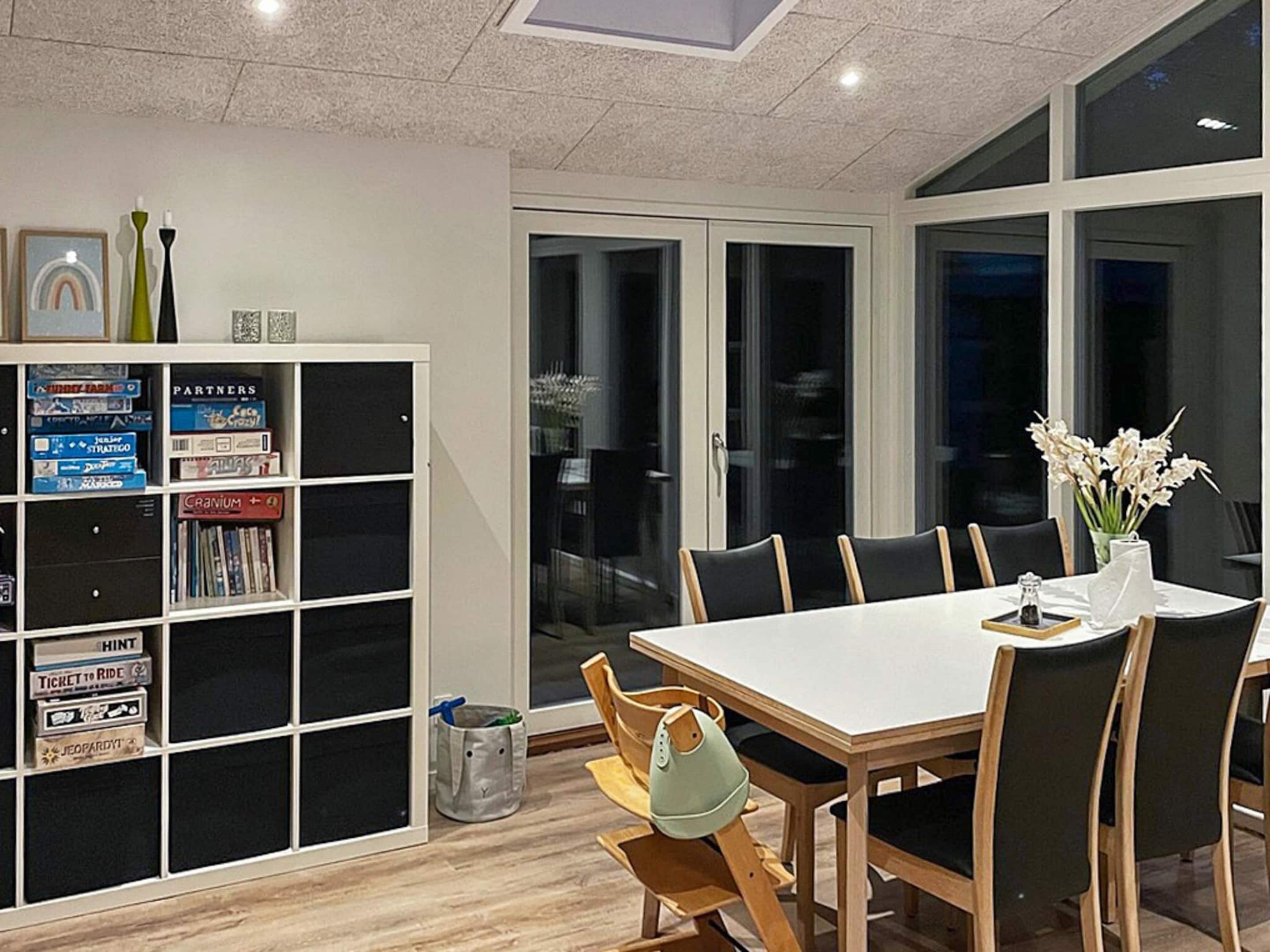 A modern dining area with a white table and black chairs, a bookshelf with various books, and a vase with flowers on the table.