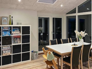 A modern dining area with a white table and black chairs, a bookshelf with various books, and a vase with flowers on the table. - 4 Star Holiday Home in Tarm (Tarm)