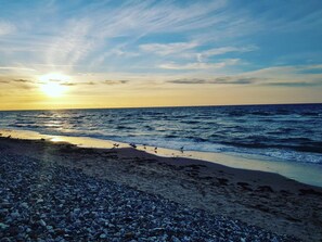 A beach with pebbles and waves, and the sun is setting in the background.