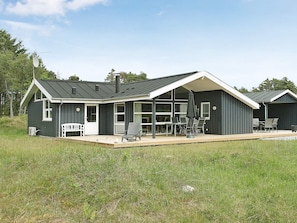 Ett modernt hus med en täckt uteplats, stora fönster och utemöbler.