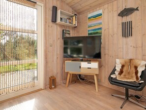 Une pièce avec un téléviseur posé sur un meuble en bois, une bibliothèque, un tableau et un fauteuil recouvert d’un plaid en fourrure.