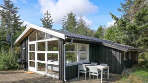 A small wooden cabin with a large windowed porch, a table, and a grill.