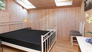 A room with a bed, skylights, a small table, and a chair.