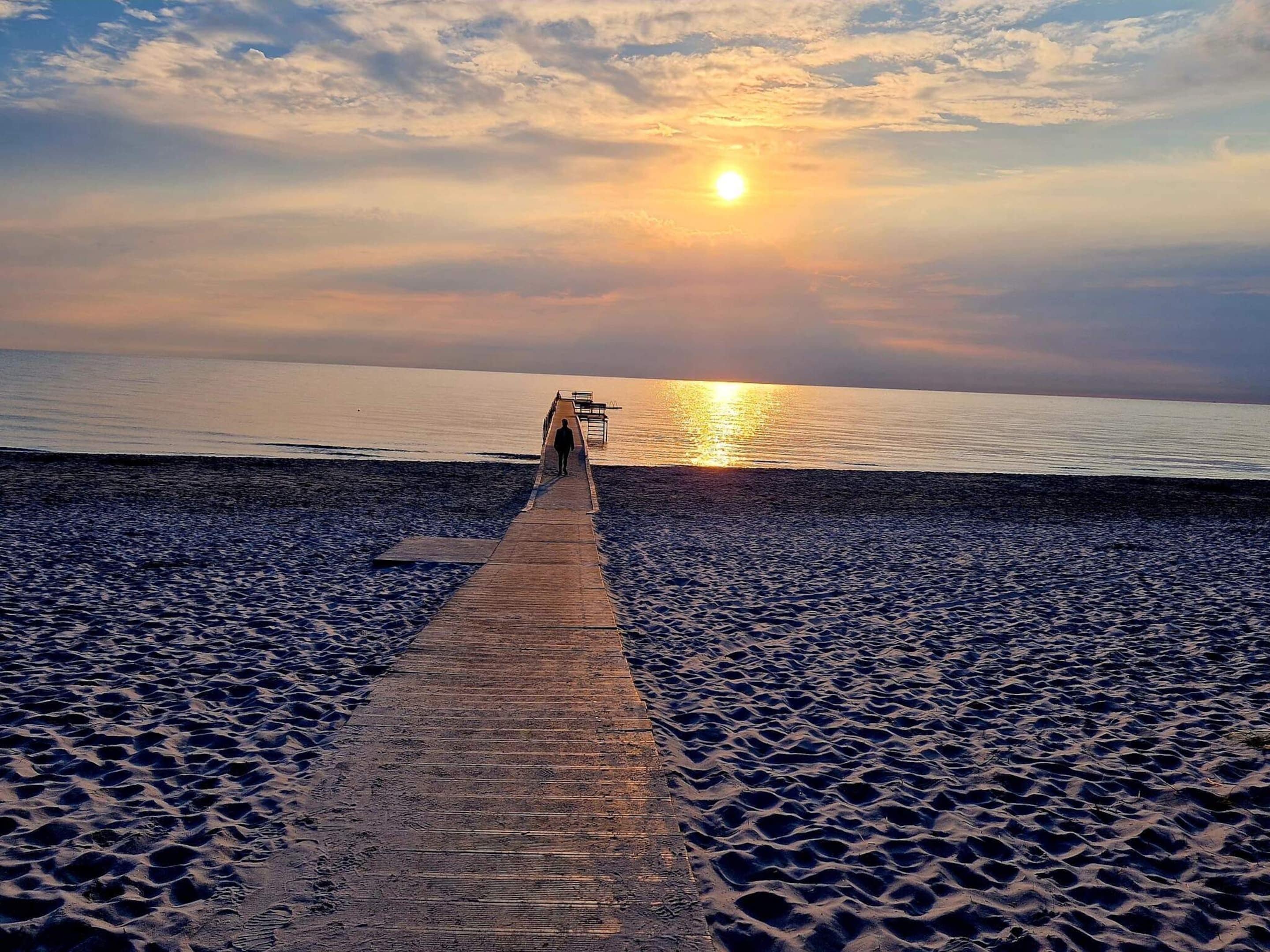 Een houten looppad dat naar een waterpartij leidt, met een zonsondergang op de achtergrond.