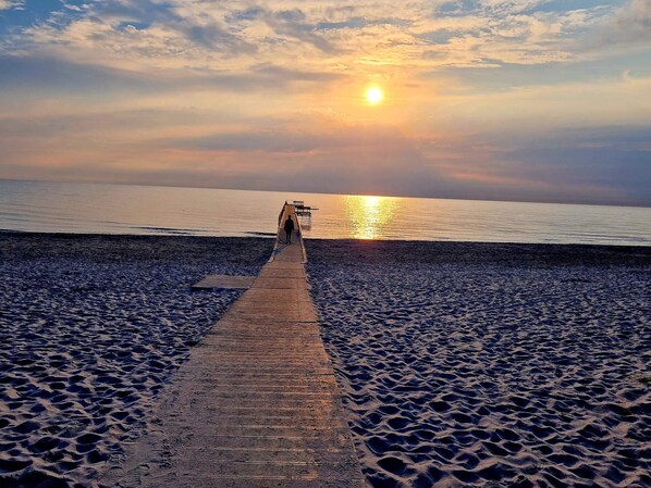 Un muelle de madera que conduce a una masa de agua con un atardecer de fondo.