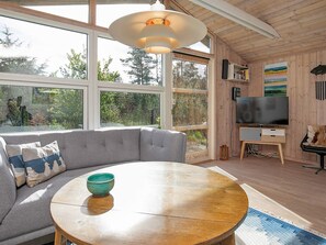 Una sala de estar moderna con un gran ventanal, una mesa redonda de madera, un sofá gris y un televisor.
