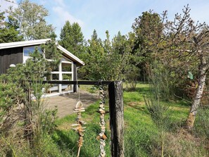 Una tanca de fusta amb un mur de pedra, una casa amb una porta de vidre, i una zona enjardinada amb arbres.