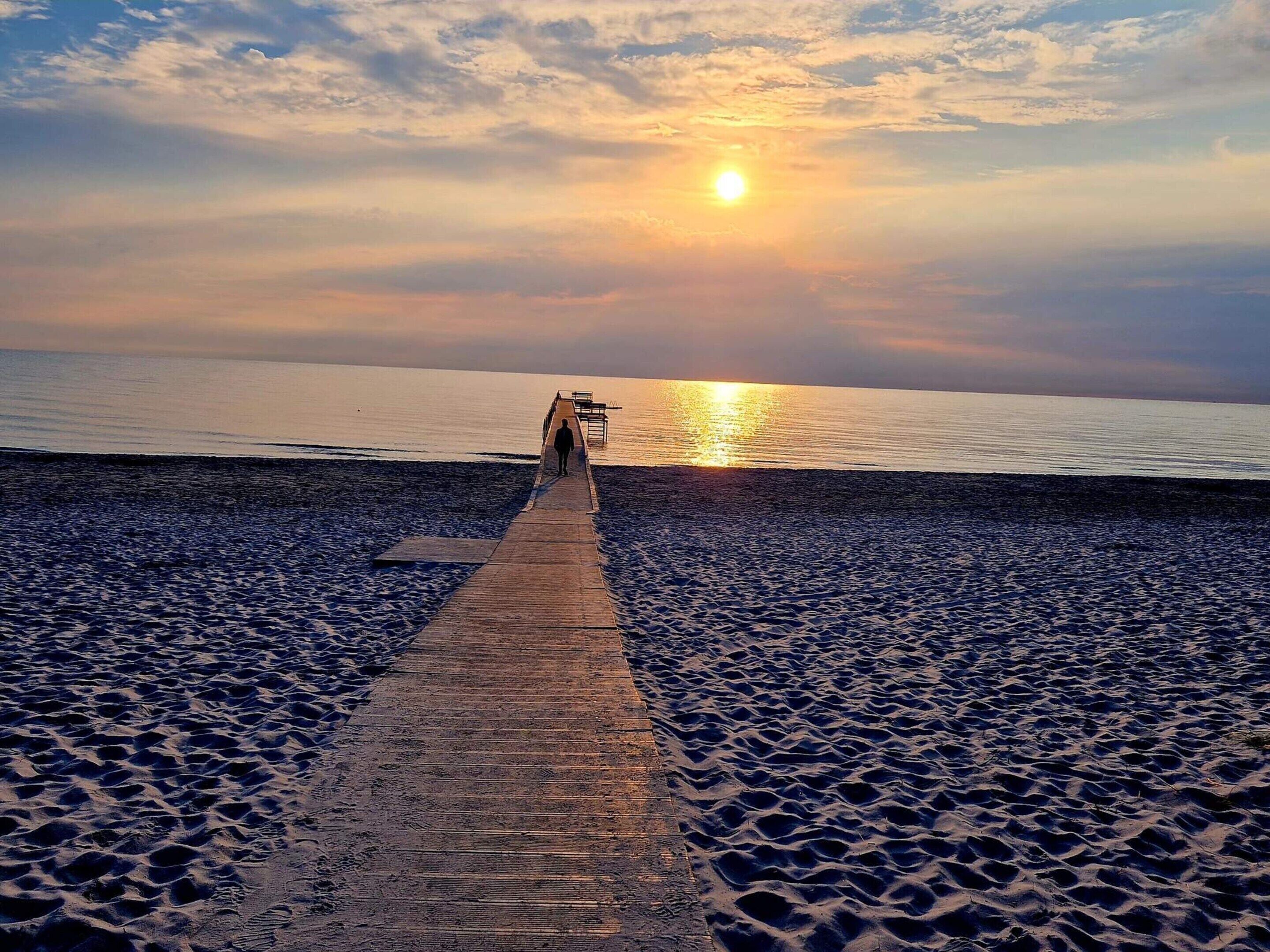 A wooden pier leading to a beach with a sunset in the background.