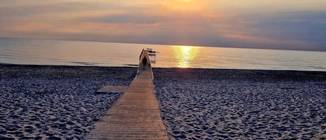 A wooden pier leading to a beach with a sunset in the background.