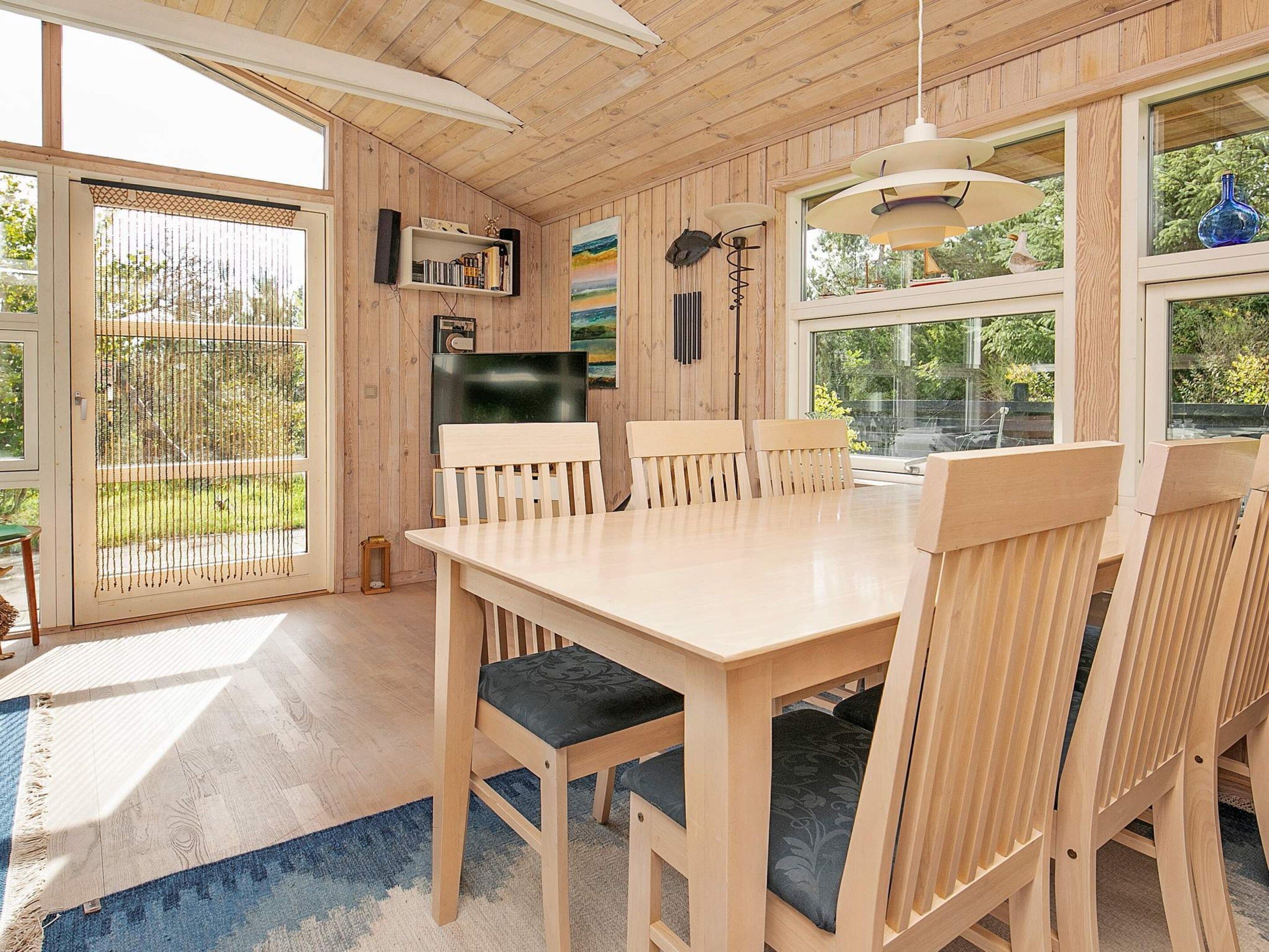 A wooden-paneled room with a dining table, chairs, a TV, and a bookshelf.