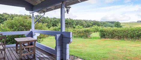 A covered outdoor area with a wooden deck, a table, and a bench.