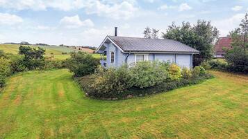 A single-story house with a gabled roof, surrounded by a well-maintained lawn and dense shrubbery.