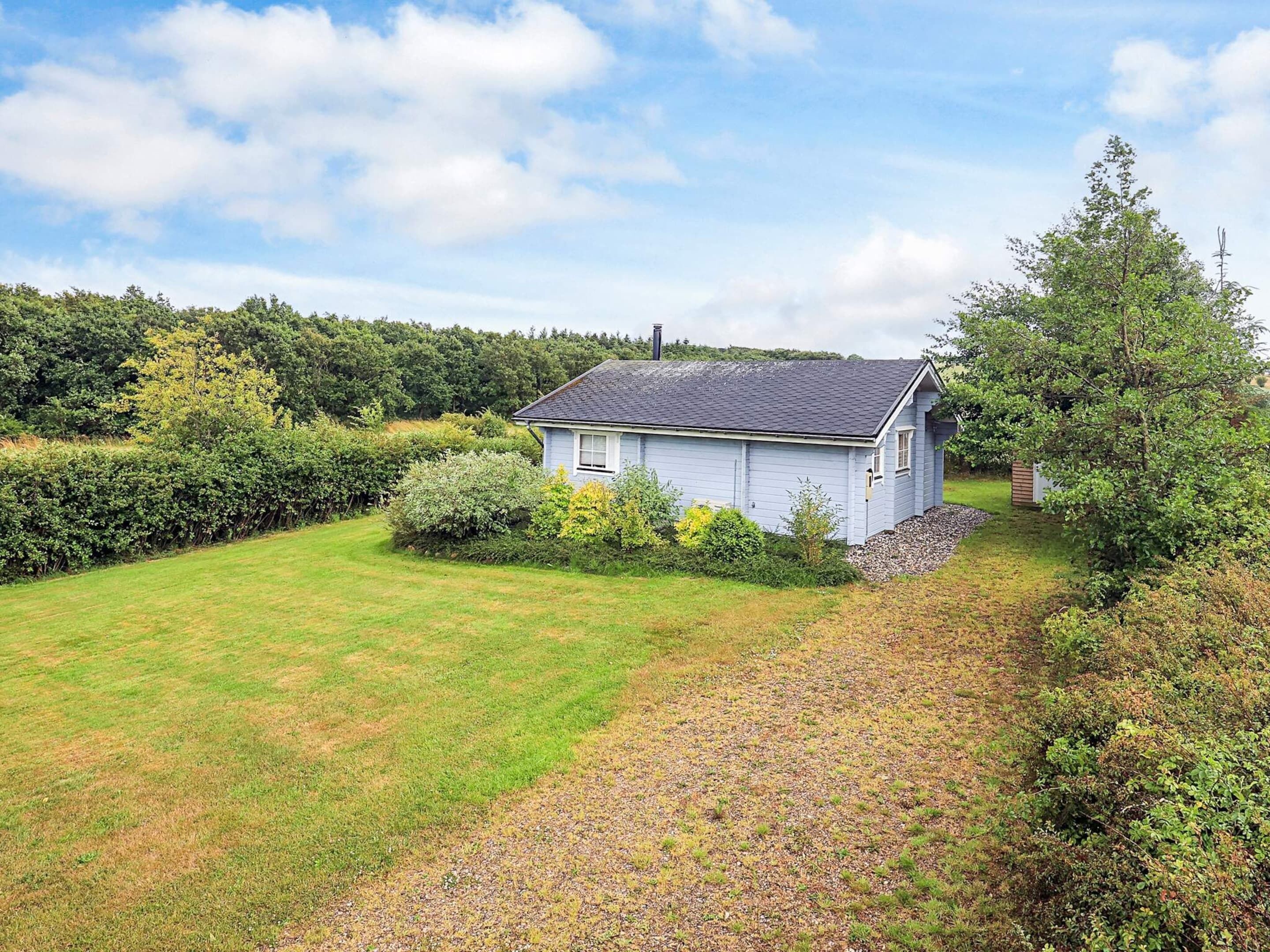 A single-story house with a sloped roof, surrounded by a well-maintained lawn and dense shrubbery.