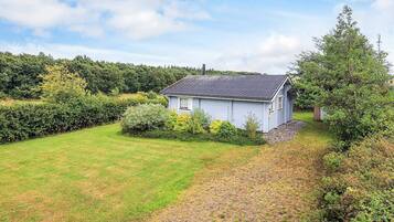 A single-story house with a sloped roof, surrounded by a well-maintained lawn and dense shrubbery.