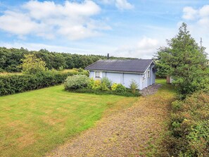 A single-story house with a sloped roof, surrounded by a well-maintained lawn and dense shrubbery. - 6 Person Holiday Home in Roslev (Roslev)