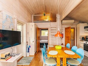 Un acogedor interior de cabaña con una mesa de comedor de madera, sillas azules, un televisor y un mapa en la pared.