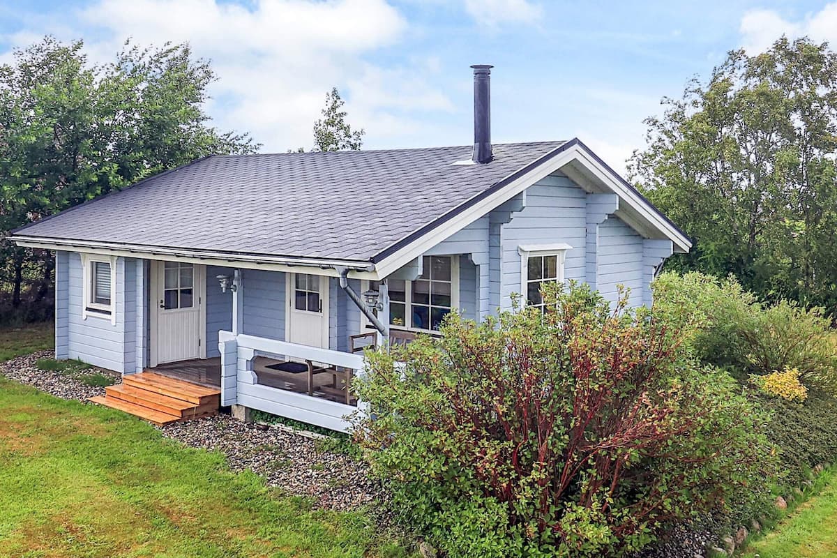 A single-story house with a gabled roof, a chimney, and a front porch with a bench.