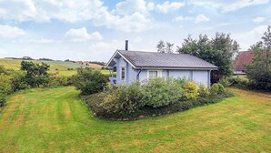 A small, single-story house with a sloped roof, surrounded by a well-maintained lawn and dense shrubbery. - 6 Person Holiday Home in Roslev (Roslev)