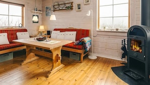 Un interior de cabaña acogedor con una mesa de madera, dos bancos tapizados en rojo, una chimenea y ventanas amplias.