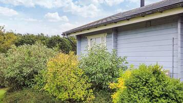 A house with a grey exterior, a chimney, and a garden with various shrubs and trees.