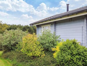 A house with a grey exterior, a chimney, and a garden with various shrubs and trees. - 6 Person Holiday Home in Roslev (Roslev)