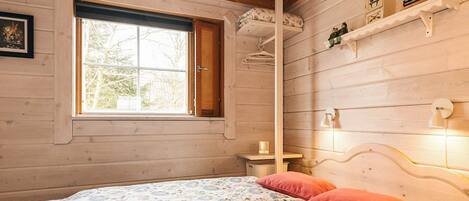 Een gezellige kamer met een bed, een raam, een plank met boeken en een wandlamp.