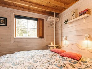 Habitació acollidora amb un llit, una finestra, una estant de llibres i una làmpada penjada a la paret.