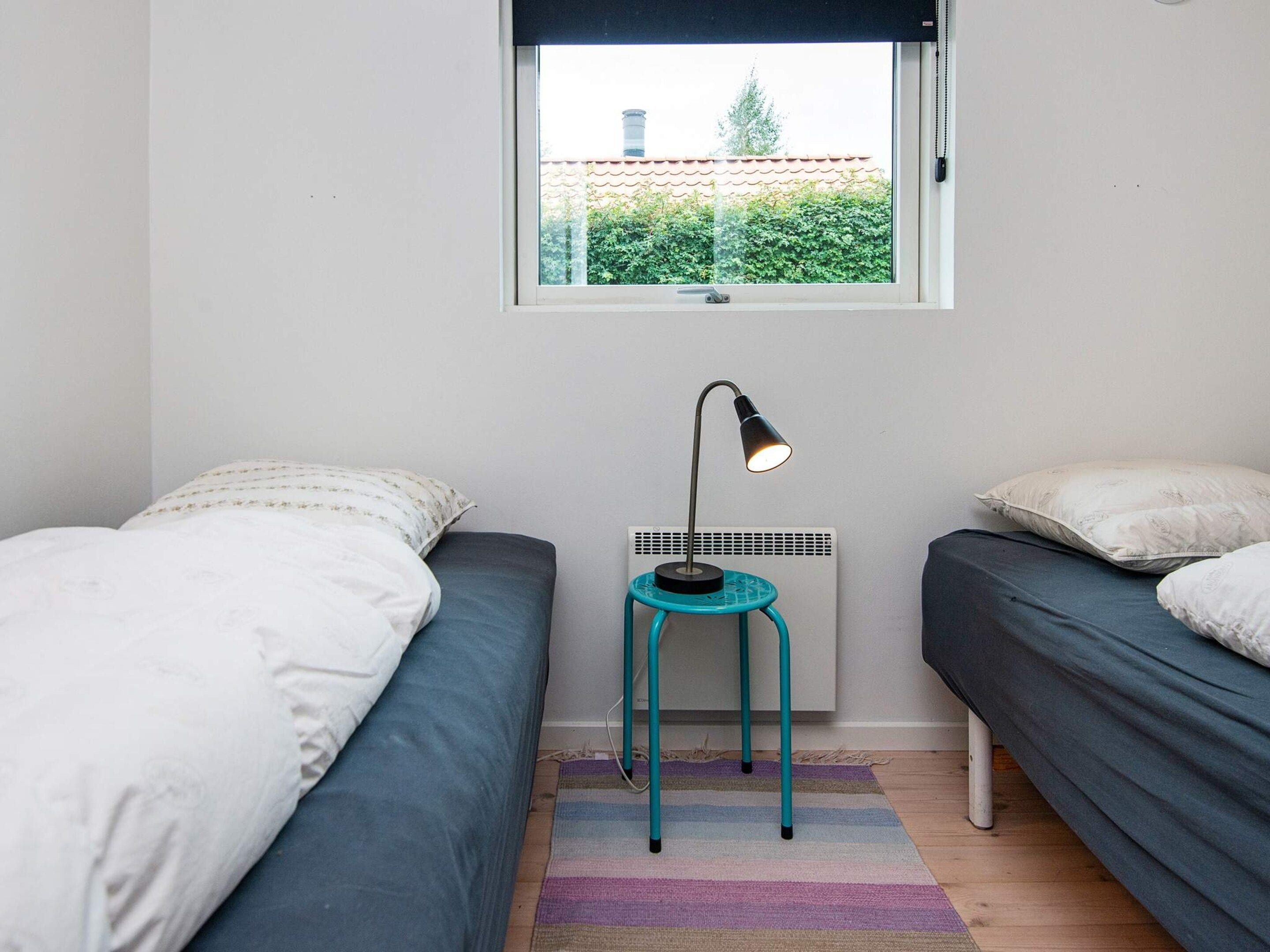 Un dormitorio con dos camas individuales, un calentador portátil, una ventana con vistas a zonas verdes y una alfombra a rayas.