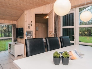 Un intérieur moderne en bois, comprenant une table à manger, des chaises, un téléviseur et une vue sur l’extérieur.