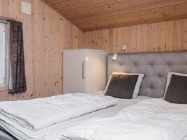A room with wooden walls, a bed with white bedding, a grey headboard, a bedside lamp, and a white wardrobe.