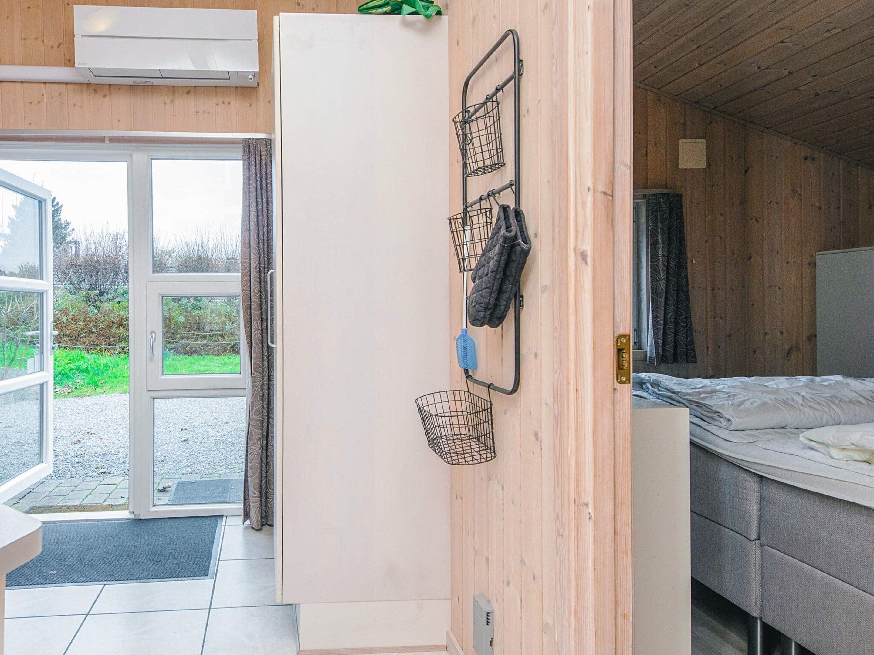 Ein Zimmer mit einem Bett, einer weißen Tür, einem Fenster und einem an der Wand befestigten Ablagefach mit Gegenständen.
