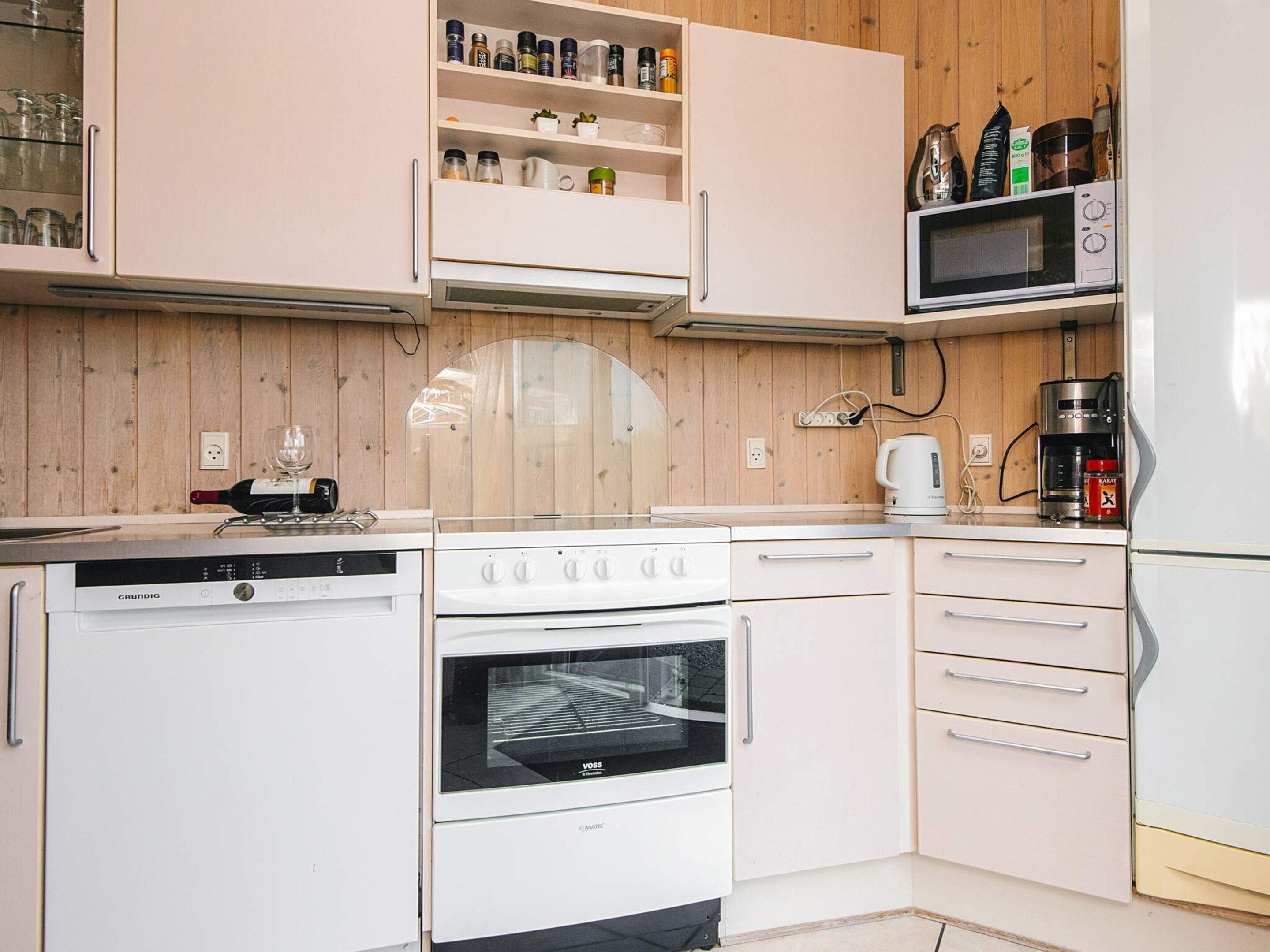 A compact kitchen with white appliances, wooden cabinetry, and a microwave on the countertop.