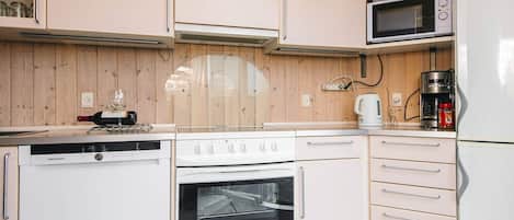 Une cuisine compacte avec des appareils électroménagers blancs, des meubles en bois et un four à micro-ondes posé sur le plan de travail.