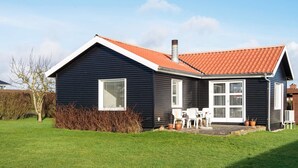 A single-story house with a dark exterior, a red-tiled roof, and a small front yard with a lawn and a tree.