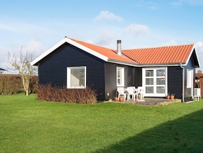 A single-story house with a dark exterior, a red-tiled roof, and a small front yard with a lawn and a tree.