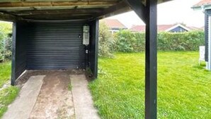 A covered outdoor area with a closed roller door, a concrete path, and a grassy lawn.