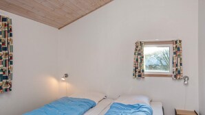 A room with two beds, a window with curtains, a wall-mounted lamp, and a small wooden shelf. - 4 Star Holiday Home in Hemmet (Hemmet)
