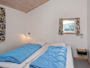 A room with two beds, a window with curtains, a wall-mounted lamp, and a small wooden shelf. - 4 Star Holiday Home in Hemmet (Hemmet)