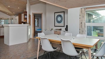 Eine moderne Küche mit weißen Schränken, einer Holzbalkendecke und einem Essbereich mit großem Tisch und Stühlen.