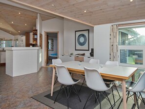 A modern kitchen with white cabinetry, a dining area with a large table and chairs, and a view of the outdoors through a large window. - 4 Star Holiday Home in Hemmet (Hemmet)