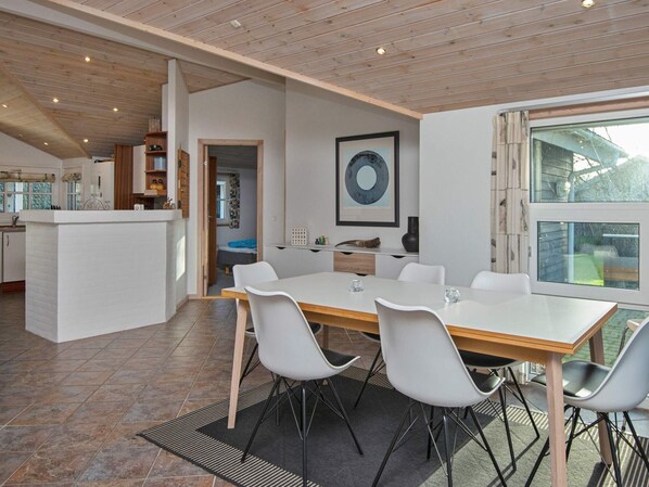 A modern kitchen with white cabinets, a wooden ceiling, and a dining area with a large table and chairs.