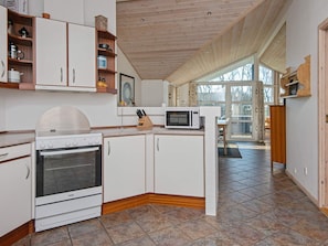 A modern kitchen with white cabinetry, a stove, a microwave, and a dining area with a view through large windows. - 4 Star Holiday Home in Hemmet (Hemmet)