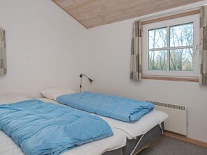 A bedroom with two beds, a window with curtains, a radiator, and a wall-mounted lamp.